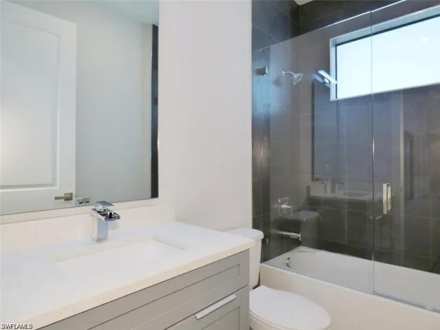 Full bathroom featuring combined bath / shower with glass door, toilet, and vanity