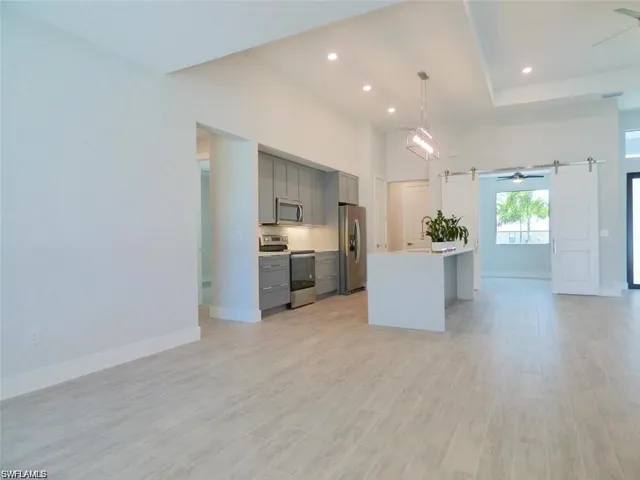 Kitchen with light hardwood / wood-style floors, stainless steel appliances, gray cabinets, a barn door, and ceiling fan