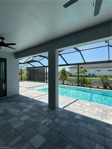 View of swimming pool featuring ceiling fan, glass enclosure, and a patio area