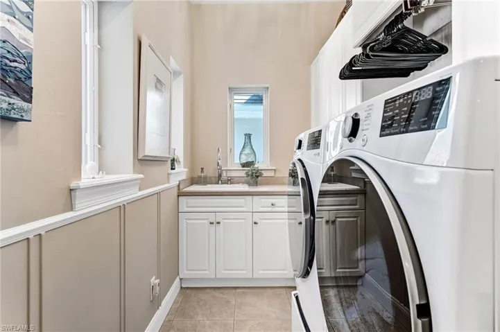 The well-appointed laundry room features generous storage, hanging space, a deep utility sink, and a front-loading washer and dryer, combining functionality with style.