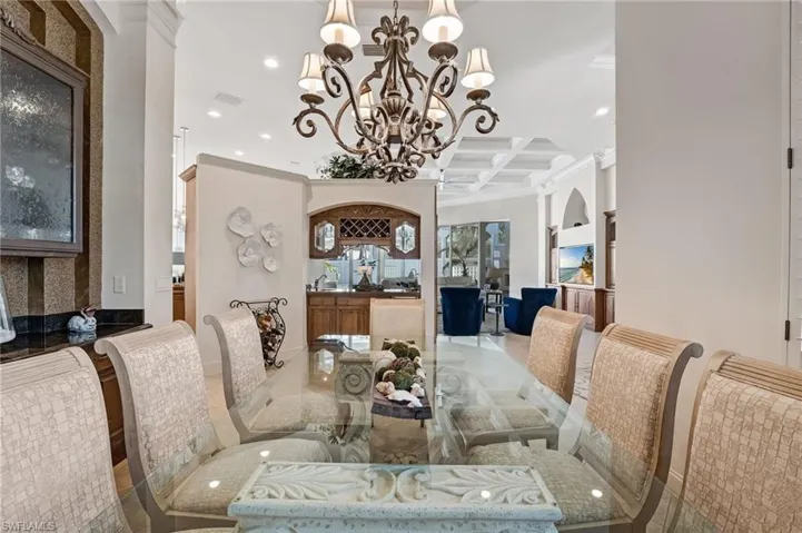 The formal dining area features a built-in buffet with frosted glass cabinetry and a stunning chandelier, while across the room, a classic wet bar with a refrigerator and bar sink provides the perfect space for entertaining guests.