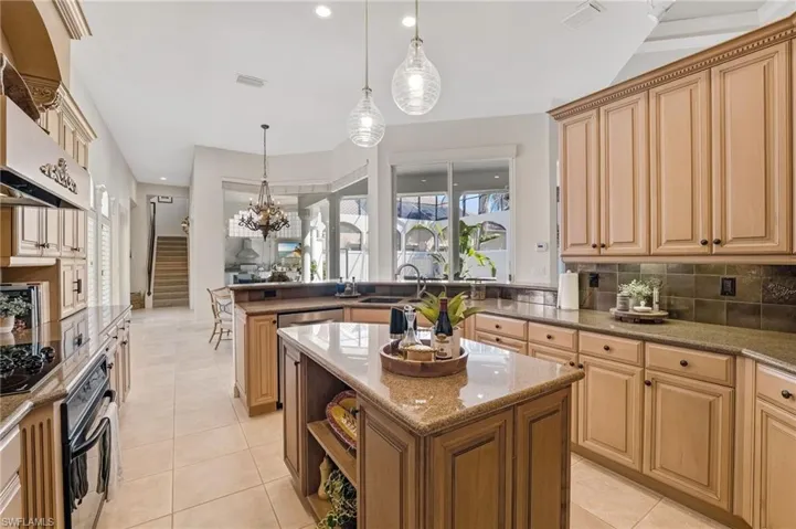 The chef’s kitchen showcases honey-toned custom wood cabinetry, granite countertops with a central island overlooking the courtyard, complemented by a stylish tile backsplash and elegant under-cabinet lighting.