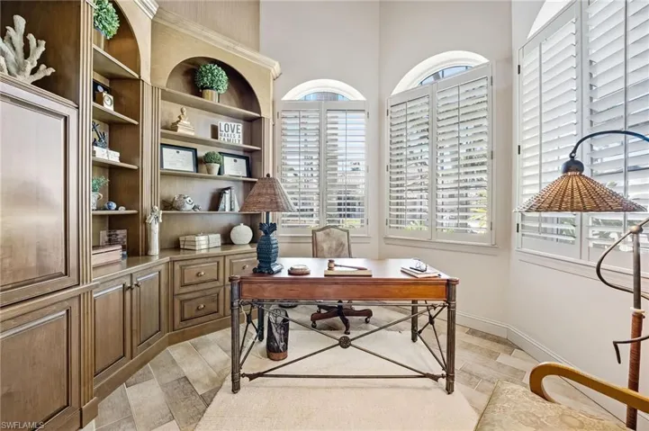 This distinguished office showcases exquisite custom wood cabinetry, abundant natural light ideal for productivity, classic plantation shutters, and a dramatic soaring coffered ceiling that elevates the space with architectural elegance—conveniently located just across the hall from the primary suite.