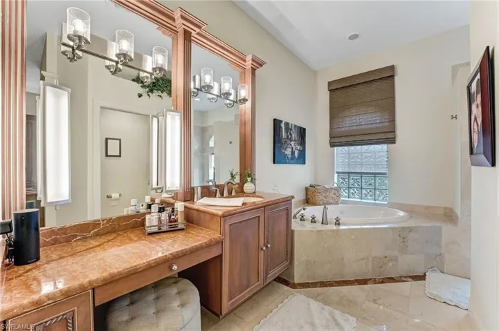 The primary bath offers separate dressing areas for him and her, two private water closets, a soaking garden tub, and a walk-through shower connecting the spaces, along with two walk-in closets. Marble countertops and custom framed mirrors complete this luxurious retreat.