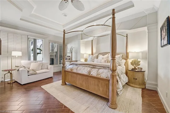 The primary suite features double tray ceilings with cloud lighting, diagonally laid tile, and plantation shutters, spacious seasting area along with direct access to the lanai. Custom wall insets with recessed lighting add a sophisticated, architectural touch.