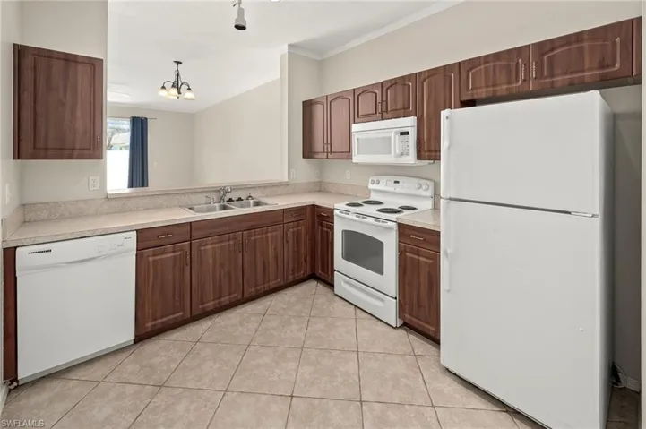 Kitchen with sink, light tile patterned floors, ornamental molding, pendant lighting, and white appliances