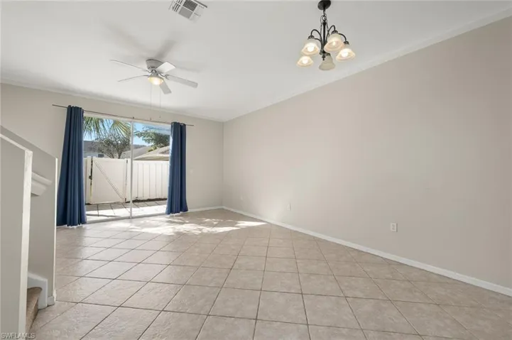 Tiled spare room featuring ornamental molding and ceiling fan with notable chandelier