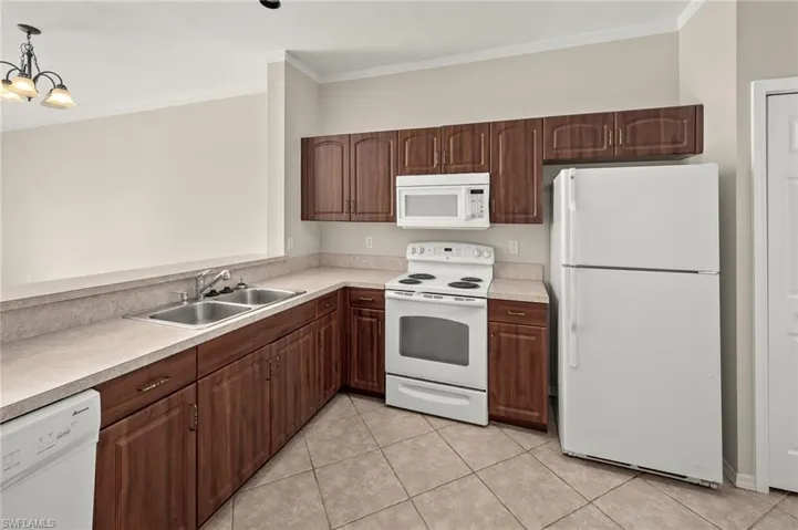 Kitchen with sink, crown molding, hanging light fixtures, light tile patterned floors, and white appliances