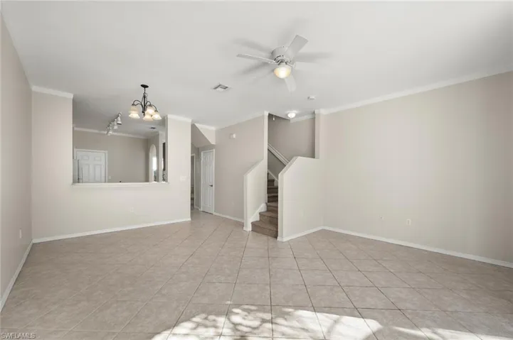 Unfurnished living room with ornamental molding, ceiling fan with notable chandelier, and light tile patterned floors