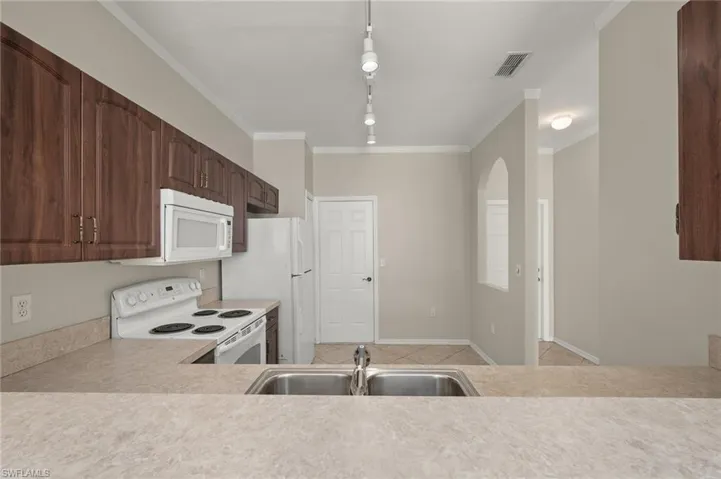 Kitchen featuring white appliances, ornamental molding, sink, and dark brown cabinetry