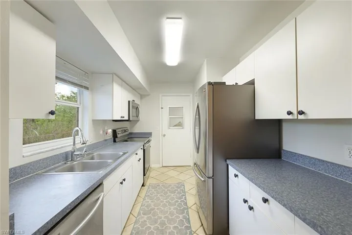 Galley kitchen featuring white cabinetry, gray speckled countertops, stainless steel appliances, a double basin sink, and tiled flooring