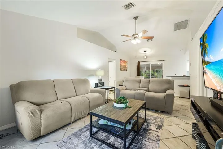 Open-concept living area featuring vaulted ceilings, ceiling fan light fixture, tile flooring, and sliding glass door access to the outdoor space