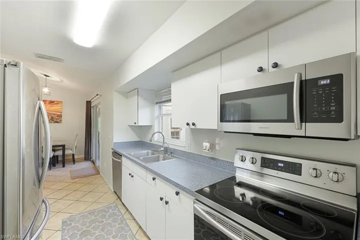Kitchen featuring white cabinetry, stainless steel appliances, a double basin sink, and wood-finish tile flooring