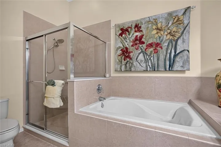Tiled bathroom featuring a built-in soaking tub and a glass-enclosed shower with a handheld showerhead