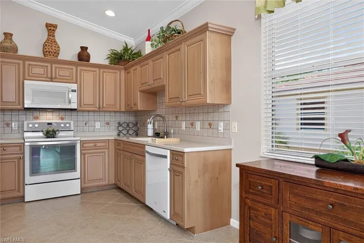 Kitchen featuring light wood cabinetry with crown molding, a tile backsplash, light-toned countertops, and integrated appliances