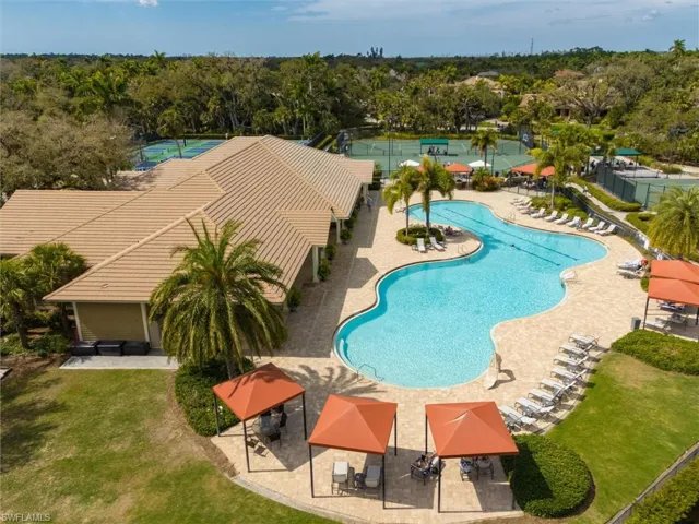Community amenity center featuring a large freeform swimming pool, extensive paved sundeck, multiple covered cabanas, and adjacent tennis courts