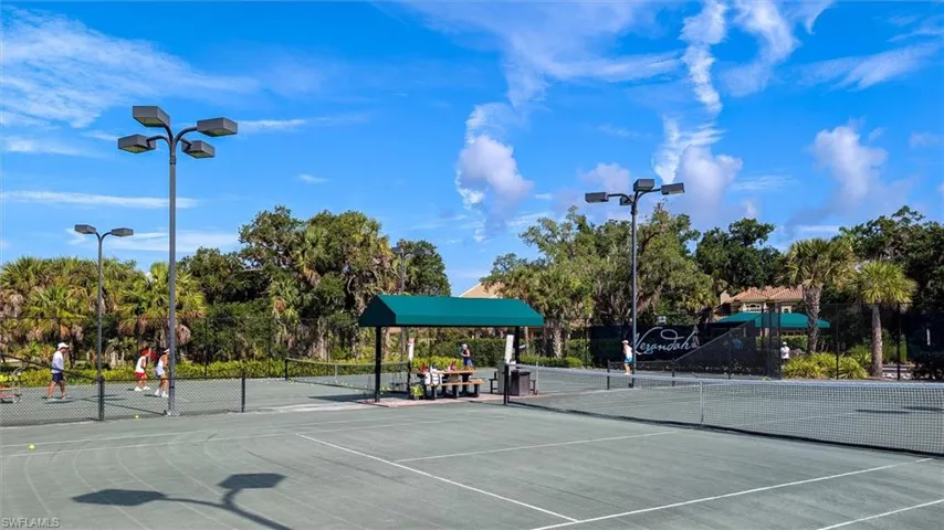 Hard-surface tennis courts featuring perimeter fencing, spectator seating, and covered picnic area