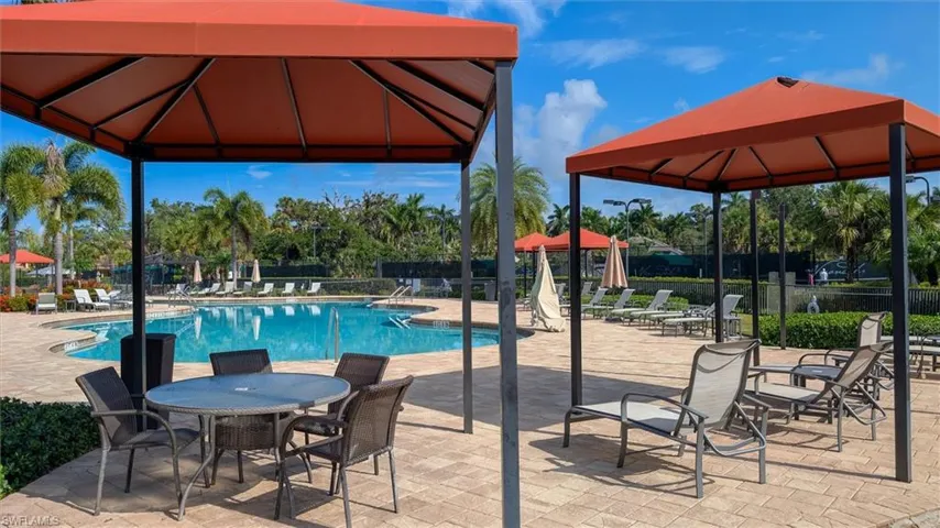 Spacious pool area featuring multiple shaded cabanas, an irregular-shaped swimming pool, a surrounding paver deck, and ample lounging space