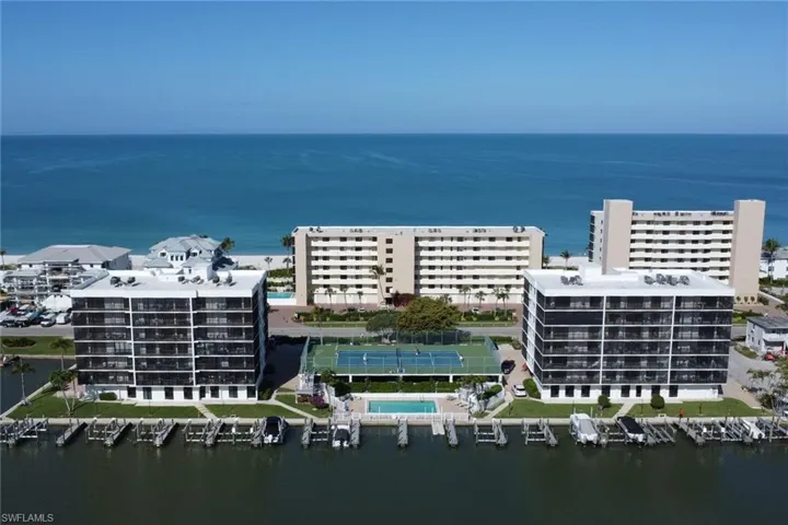 Waterfront condominium complex featuring multiple buildings with screened balconies, a marina with boat slips, a tennis court, and an outdoor swimming pool