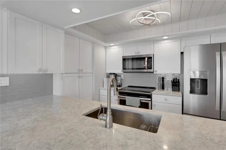 Contemporary kitchen featuring a large undermount sink with a gooseneck faucet, light-toned countertops, white shaker cabinetry, stainless steel appliances, and a subway tile backsplash