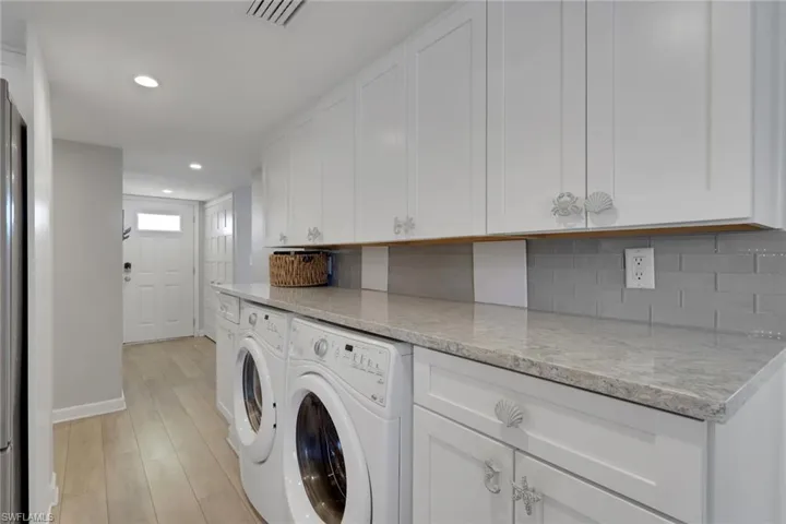 Dedicated laundry area featuring white shaker-style cabinetry, a light-toned countertop, and a gray subway tile backsplash