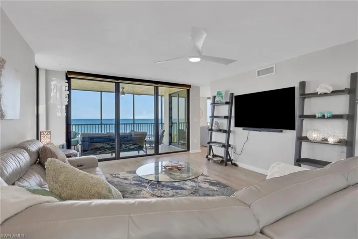 Spacious living area featuring floor-to-ceiling sliding glass doors, light wood-finish flooring, and a contemporary ceiling fan