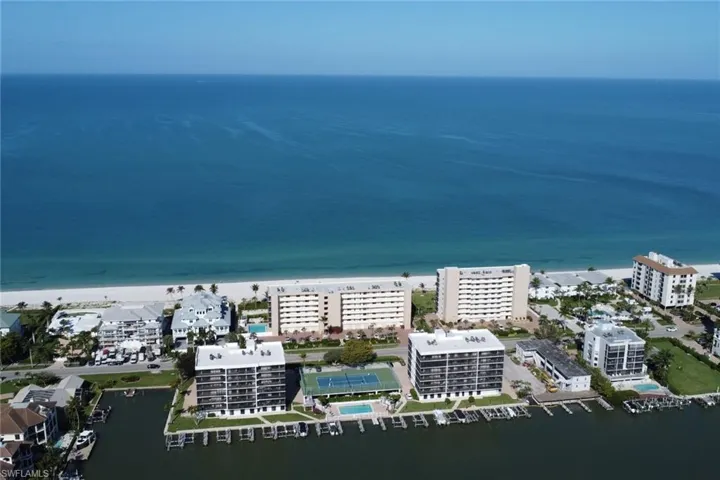 Coastal property featuring direct beach access, multiple residential buildings, private boat docks, a tennis court, and an outdoor swimming pool