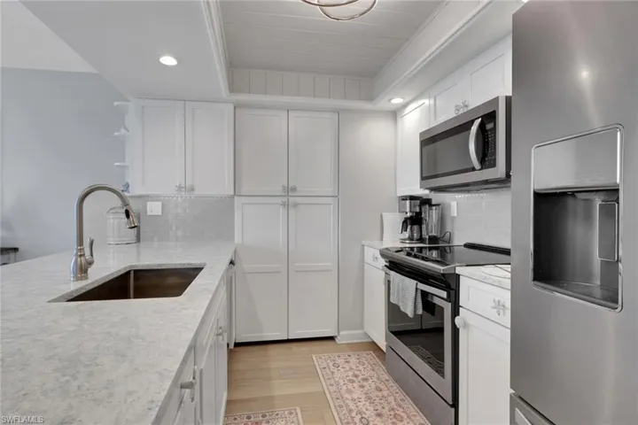 Bright kitchen featuring white cabinetry, light-toned countertops, stainless steel appliances, and a tile backsplash