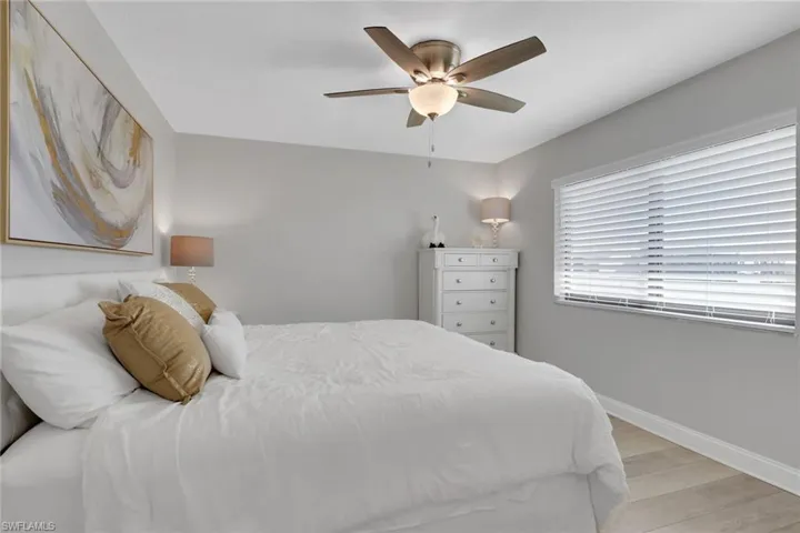 Bedroom featuring a ceiling fan with integrated lighting, wood-finish flooring, a window with horizontal blinds, and a neutral wall color