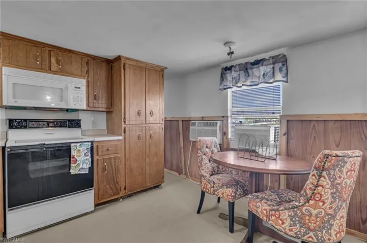 Kitchen with brown cabinets, light countertops, white microwave, an AC wall unit, and range with electric cooktop