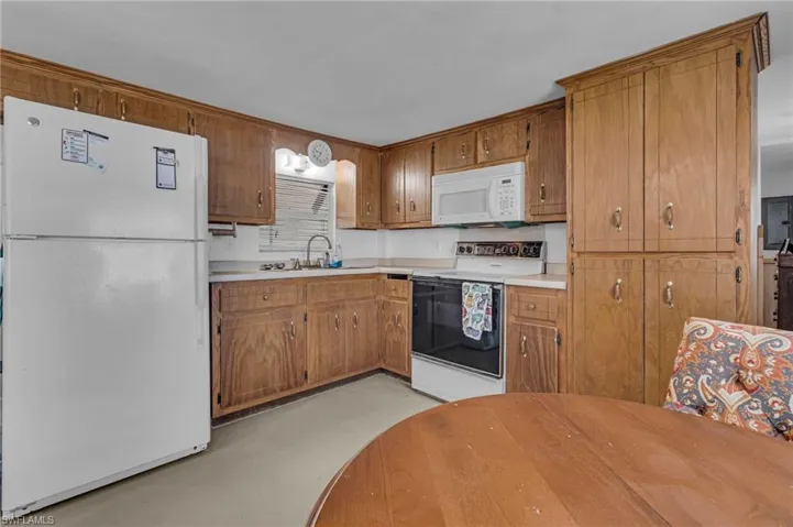 Kitchen featuring brown cabinetry, white appliances, light countertops, and a sink