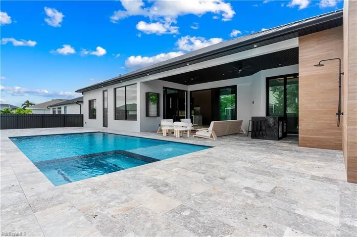 Expansive outdoor living area featuring a rectangular pool with integrated spa, large format natural stone pavers, a covered patio with recessed lighting, and a private outdoor shower