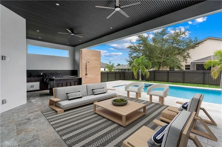 Expansive covered patio featuring a built-in outdoor kitchen with bar seating, integrated ceiling fans, and a tiled floor