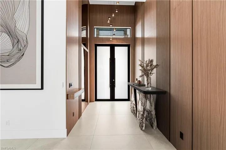 Entryway featuring extensive wood-finish paneling, light-toned tile flooring, and a contemporary pendant light fixture