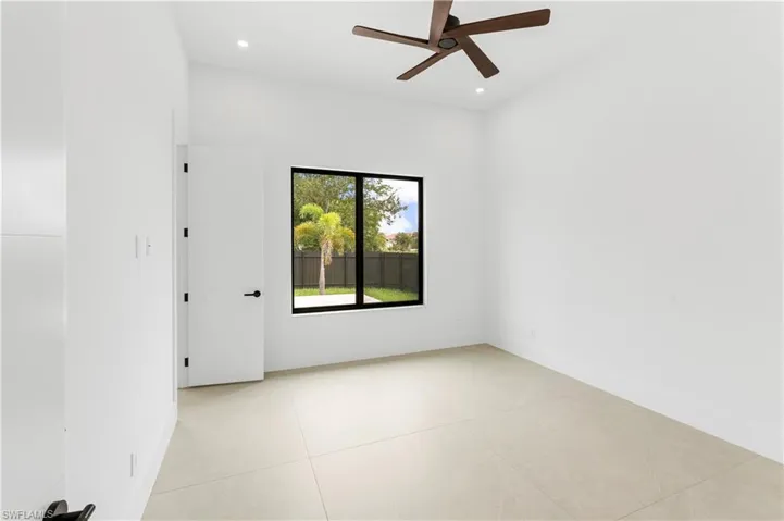 Recessed lighting, wood-finish ceiling fan, large window with black frame, light-toned tile flooring, and a modern interior door with horizontal paneling