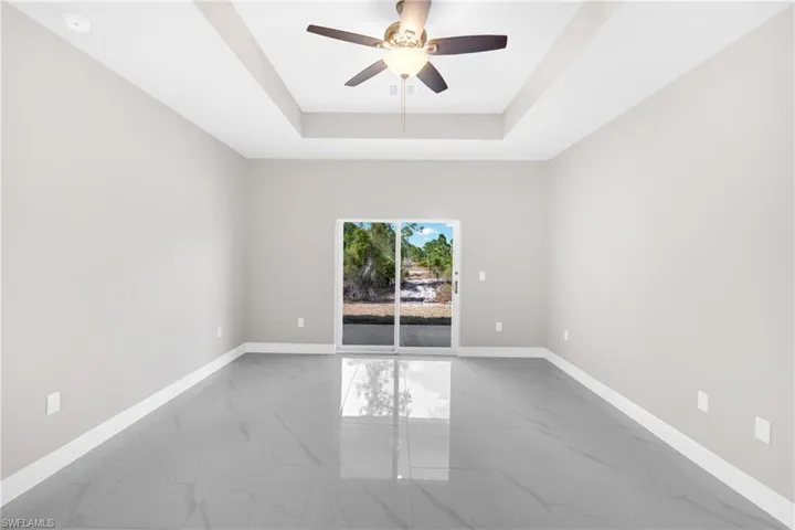 Spare room featuring light marble finish flooring, a ceiling fan, and a tray ceiling
