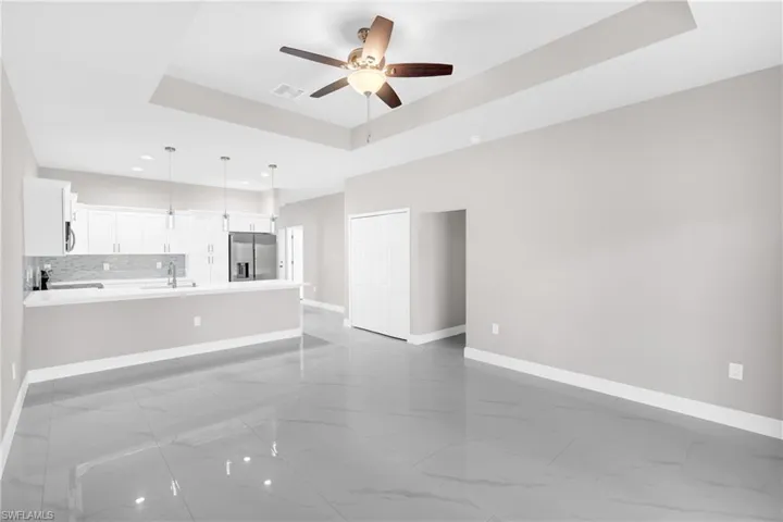 Unfurnished living room featuring a raised ceiling, ceiling fan, recessed lighting, and light marble finish flooring
