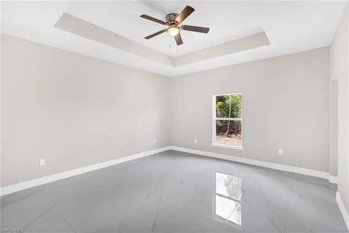 Spare room featuring ceiling fan, light marble finish floors, and a tray ceiling