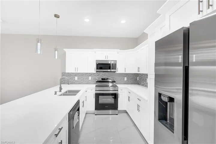 Kitchen featuring stainless steel appliances, light marble finish floors, pendant lighting, and white cabinetry