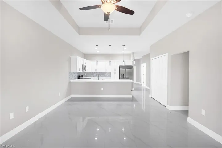 Unfurnished living room with ceiling fan, light marble finish flooring, and a raised ceiling