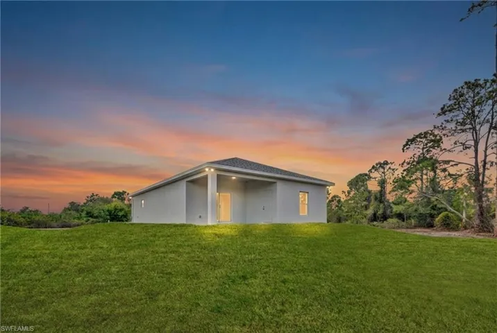 Back of property at dusk with a lawn and stucco siding
