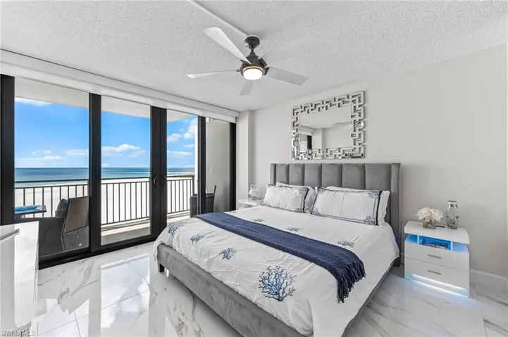Bedroom with expansive windows, light marble finish floors, access to exterior, a water view, and a textured ceiling
