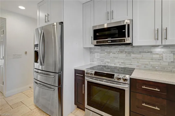 Angled view of kitchen with its tasteful mixture of kitchen cabinet colors, and tiled backsplash