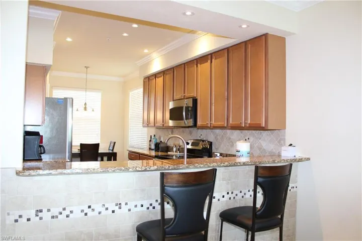Kitchen featuring ornamental molding, tasteful backsplash, light stone counters, decorative light fixtures, and brown cabinetry