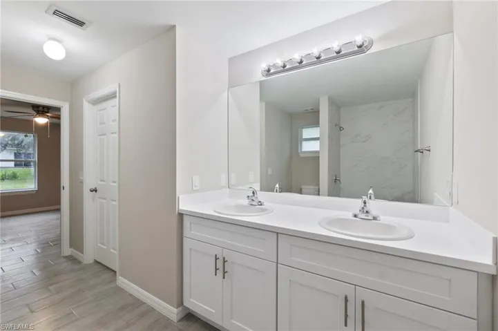 Bathroom with toilet, wood-type flooring, vanity, a tile shower, and ceiling fan