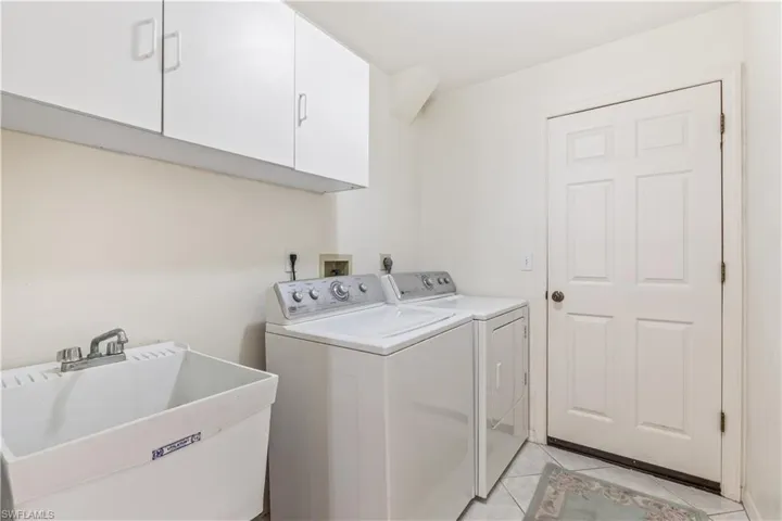 Laundry area with independent washer and dryer, electric dryer hookup, light tile floors, sink, and cabinets