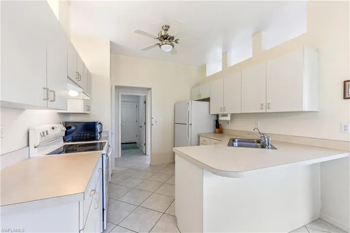 Kitchen featuring white appliances, kitchen peninsula, sink, ceiling fan, and light tile floors