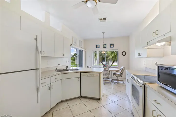 Kitchen with ceiling fan, white appliances, light tile flooring, hanging light fixtures, and sink