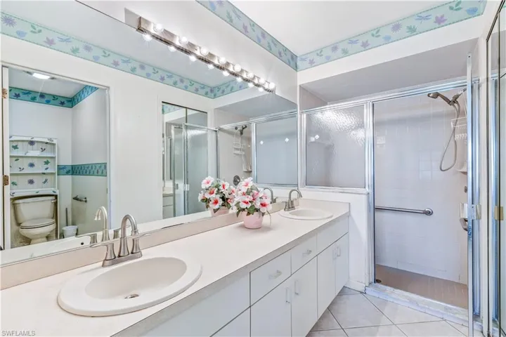 Bathroom featuring double sink vanity, a shower with shower door, toilet, and tile floors