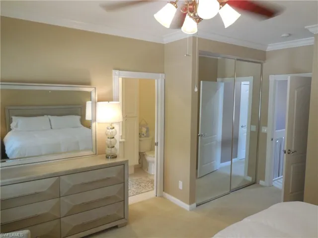 Bedroom with crown molding, light colored carpet, ensuite bath, baseboards, and a closet